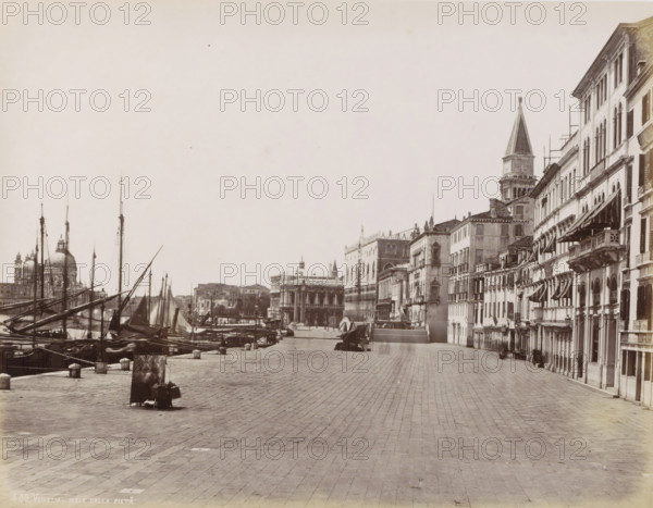 Quay in Venice seen towards St. Mark's Square, Quai des Esclavons à Venise, Venezia - Molo dalla Pietà, photograph, Part of Topographical album of Venice 1881., negative number: '400', check stamp: 'Carlo Ponti Venezia', photographer: Carlo Ponti, Venice, 1860 - 1881, Carlo Ponti, photographer, paper, albumen print, height 200 mm x width 259 mm, quay (city(-scape) with figures, staffage), tower, clock tower, monumental adornment, Roman Catholic Church, travel, A wide riverside promenade paved with large rectangular stones runs along the right side of the image, bordered by a row of multi-story buildings with arched windows, balconies, and striped awnings, while to the left several moored wooden boats with tall masts and rigging line the water's edge; in the distance a domed church and a tall bell tower rise above the cityscape, and a colonnaded building stands near the waterfront, all under a pale sky.