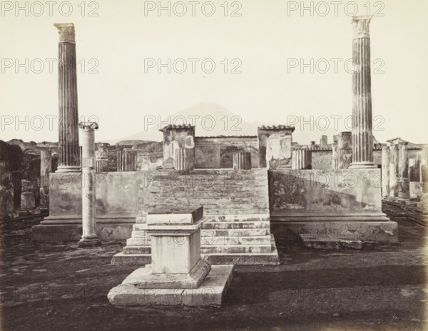 Pompeii: Temple Venus: searches 1817., Remains of the Temple of Venus in Pompeii with Mount Vesuvius in the background, photograph, Part of Travel album with photos of sights in Naples and surroundings., negative number: '6560', c. 1865 - c. 1875, photographer, paper, albumen print, albumendruk, height 208 mm x width 253 mm, column, pillar, architecture, temple, shrine, non-Christian religions, excavation, archeology, A wide view of ancient stone ruins centered on a stepped platform leading up to a raised terrace with low walls and remnants of painted plaster, flanked by tall fluted columns with ornate capitals and shorter broken column stubs, with a solitary slender column standing in the foreground on a square base and a rectangular plinth positioned at the base of the steps, all set on a dark textured ground and with distant low hills visible against a pale sky.