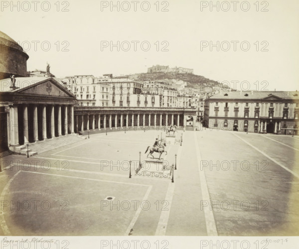Piazza del Plebescito with equestrian statues in Naples, Piazza del Plebescito, photograph, Part of Travel album with photos of sights in Naples and surroundings., Naples, c. 1865 - c. 1875, photographer, paper, albumen print, albumendruk, height 199 mm x width 252 mm, equestrian statue, square, circus, etc. (city(-scape) with figures, staffage), A wide pale plaza with tiled paving is flanked by a large classical building with a columned portico and a triangular pediment on the left and a long colonnade curving across the middle ground, with multi-story buildings rising behind them; three equestrian statues mounted on raised plinths stand along the plaza center, each surrounded by short posts and chains and paired with tall street lamps; a broad open roadway runs along the right side toward a rectangular building with arched entrances and evenly spaced windows; in the distant background a hillside with layered buildings and a prominent fortress-like structure sits beneath a pale sky.
