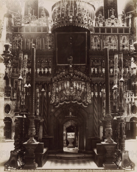 Intérieur du St.-Sépulcre avec ornements. - Interior of the Holy Sepulcher with ornaments., Interior of the Church of the Holy Sepulcher in Jerusalem, photograph, Part of Travel album with photos of Jerusalem and other biblical places., inscription: '...ves No. 74', negative number: '850', photographer: Maison Bonfils, Jerusalem, c. 1867 - c. 1895, pasteboard, paper, albumen print, height 282 mm x width 225 mm, interior of church, Church of the Holy Sepulchre, A large ornate interior view filled with carved columns, tall decorative poles, hanging lamps, and intricately patterned panels; a central dark archway framed by twisted pillars leads inward toward a smaller altar piece visible through the opening, while above the arch are rows of ornate metalwork, suspended lamps, and sculpted reliefs; flanking the central opening are tall painted columns and carved pedestals topped with finials and cone-shaped covers, and the upper portion shows framed panels with figural images and floral deco...