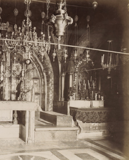 XII et XIII Stations, le Calvaire, autel grec.- places., negative number: '270', photographer: attributed to Maison Bonfils, Church of the Holy Sepulchre, c. 1867 - c. 1895, Jerusalem, Attributed to, pasteboard, paper, albumen print, height 224 mm x width 283 mm, altar, stations of the cross, Church of the Holy Sepulcher, A sepia-toned interior photograph showing an ornate religious space with hanging lamps and elaborate metal chandeliers suspended from the ceiling, a decorative archway with radiating carved elements, carved columns, candleholders with tall candles, an altar draped with patterned cloth, a statue or carved figure seated within a niche, floral garlands around a framed decorative panel, intricate metalwork and chains, stone steps and a tiled floor with geometric patterns.
