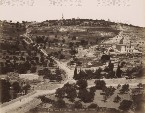 View of the Mount of Olives in Jerusalem, Mont des Oliviers. - The Mount of Olives., photograph, Part of Travel Album with photos of Jerusalem and other biblical places., negative number: '292', photographer: Maison Bonfils, Jerusalem, c. 1867 - c. 1895, pasteboard, paper, albumen print, height 223 mm x width 281 mm, mountains (landscape with figures, staffage), Mount of Olives, A wide sepia-toned landscape showing a hilly terrain with scattered trees and winding dirt paths leading upward, stone terraces and low walls breaking the slopes, a cluster of buildings on the right including a multi-domed ornate structure and adjacent rectangular buildings, ruins and small stone structures dotting the midground, taller tower-like structures visible on the ridge in the distance, and a foreground with more trees, stone enclosures, and a curved road.