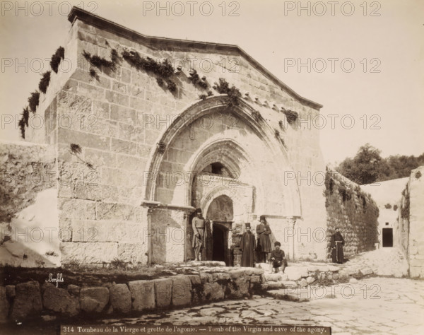 Tomb of the Virgin Mary and the Cave of the Agony in Jerusalem, Tombeau de la Vierge et grotte de l'agonie. - Tomb of the Virgin and cave of the agony., photograph, Part of Travel album with photos of Jerusalem and other biblical places., negative number: '314', photographer: Maison Bonfils, Jerusalem, c. 1867 - c. 1895, Maison Bonfils, photographer, pasteboard, paper, albumen print, height 225 mm x width 284 mm, church (exterior), grave, tomb, cave, grotto, A stone building facade with a large arched entrance and smaller arched recesses, weathered block masonry and patches of vegetation growing on and along the upper walls; a cobbled foreground with low stone steps and a raised stone platform; several men in long garments and hats gathered near the entrance, one seated on the steps and others standing; a narrow passage to the right lined by a high stone wall topped with foliage and a distant dark doorway; pale sky above.