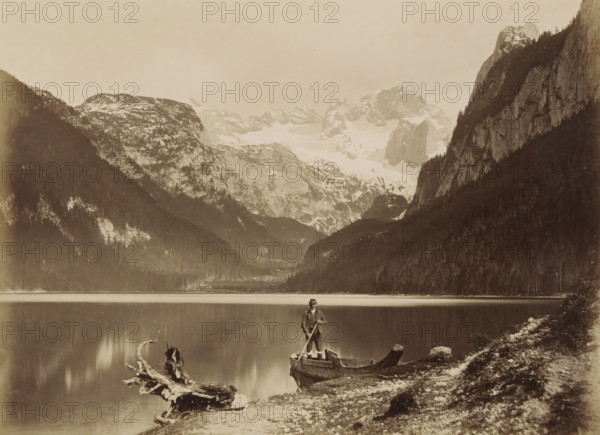 View of a lake and surrounding mountains with a man standing in a boat in the foreground, presumably in the Alps, photograph, Part of a travel album with photos of sights in Germany and Austria and of works of art., Alps, c. 1870 - c. 1900, photographer, paper, albumen print, height 193 mm x width 267 mm, mountain-top, peak (landscape with figures, staffage), A sepia-toned landscape showing a still lake bordered by steep forested slopes and rocky cliffs with snow-capped mountains in the background; a man wearing a hat and coat stands in a wooden boat at the lake edge holding a pole, with a large weathered log lying on the shoreline and scattered rocks and grassy patches along the foreground.