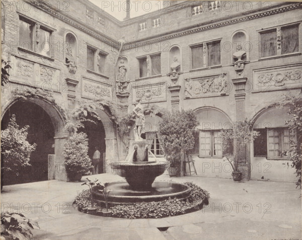 Courtyard of the castle of Pierrefonds, album page, photomechanical print, This print is part of an album., maker: Angerer & Göschl, C., 1880 - 1900, paper, autotype, height 201 mm x width 248 mm, courtyard, castle, Pierrefonds, Castle of Pierrefonds, A stone courtyard with arched walkways and a two-story brick facade featuring ornamental relief panels and recessed niches holding sculpted busts and figures, a central multi-tiered fountain with a statue atop a pedestal and water spouts, surrounding low circular planting bed with foliage, potted shrubs and small trees placed near the walls, shuttered windows and doorways beneath the arches, climbing plants and vines on the masonry, and decorative balustrade and cornice details along the upper edge of the building.