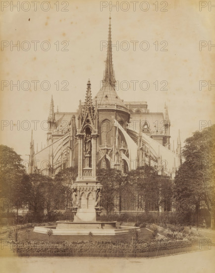 Apse of Notre-Dame of Paris, album page, photograph, This photo is part of an album., inscription: '1181 Paris _ Apside de Notre-Dame', photographer: X phot., 1887 - 1910, paper, albumen print, height 274 mm x width 209 mm, parts of church exterior and annexes: apse, Paris, Notre-Dame (Paris), A sepia-toned photograph shows a large Gothic cathedral viewed from a garden area, with an ornate stone fountain and tall sculpted monument in the foreground. The cathedral features flying buttresses, pointed arches, tracery windows, pinnacles, and a tall central spire rising above a rounded roof structure. The fountain monument has carved figures set into niches and decorative detailing on its base, and it sits within a low octagonal basin surrounded by a manicured lawn and flowerbeds. Trees frame the cathedral on both sides, and a low ornamental fence runs along the front edge of the garden. The sky above is pale and mottled.