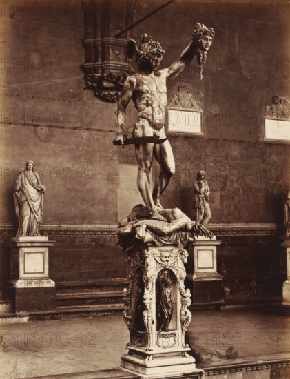Sculpture Perseus by Benvenuto Cellini in the Loggia de Lanzi in Florence, Italy, Il Perseo del Cellini, Firenze, photograph, number: '3087.', address: 'GIACOMO BROGI, FOTOGRAFO-EDITORE, FIRENZE, ', photographer: Giacomo Brogi, Florence, after sculpture by Benvenuto Cellini, 1856 - 1881, Benvenuto Cellini, after sculpture by, Tuscany, pasteboard, paper, albumen print, height 469 mm x width 351 mm, piece of sculpture, reproduction of a piece of sculpture, Toscane, Loggia dei Lanzi, A large bronze statue of a muscular male figure stands on an ornate pedestal, the figure holding a severed head aloft in one hand and a curved sword in the other, a draped, reclining body lies beneath his feet on the pedestal, the pedestal is highly decorated with sculpted figures and ornamental motifs, a tall stone wall with plaques and architectural reliefs forms the background, two additional standing statues on plinths flank the central sculpture at either side, the scene is rendered in a sepia photograph...