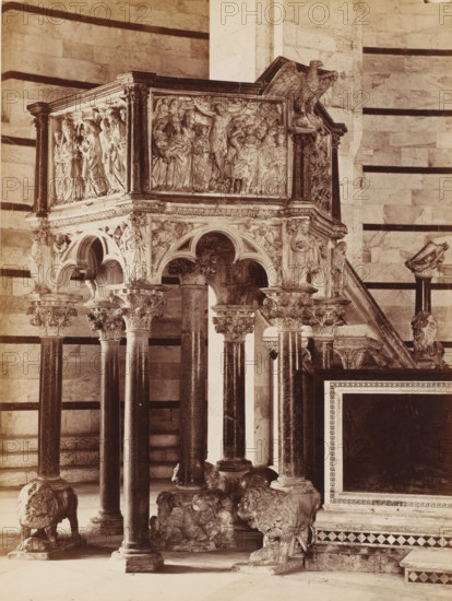 Pulpit in the Baptistery of Pisa, Italy, photograph, address: 'GIACOMO BROGI, PHOTOGRAPHEDITORE, FIRENZE, LUNG ARNO DELLE GRAZIE 15', inscription: 'PULPITO DEL BATTISTERO, PISA', photographer: Giacomo Brogi (possibly), Pisa, photographer: Carlo Brogi (possibly), publisher: Edizioni Brogi, Florence, after sculpture by Nicola Pisano, 1864 - 1900, Nicola Pisano, after sculpture by, Tuscany, pasteboard, paper, albumen print, albumendruk, height 470 mm x width 351 mm, pulpit, ambo, chancel, Baptisterium (Pisa), A stone pulpit supported on slender dark marble columns with ornate carved capitals sits above sculpted lion bases, the pulpit sides richly carved with high relief figures and scenes including draped standing figures and a central crucified figure, topped by an eagle sculpture at one corner; pointed arches and decorative molding run beneath the relief panels, and carved angels and other figures appear on the supporting arches and corner pilasters, all set against a background of hori...