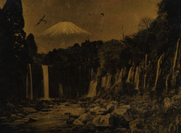 View of Mount Fuji with waterfalls, photograph, Japan, printer (person): attributed to Hanbeh Mizuno, Yokohama, 1890 - 1920, photographer, printer (person), Kanagawa, Honshu, Attributed to, plant material, biological material, inorganic material, wood (plant material), metal, lacquer photo, photography on Japanese lacquerware, height 110 mm x width 145 mm, waterfall, mountains, Fuji, A landscape dominated by a large, snow-capped mountain in the background with a conical peak; in front of it a dense dark treeline stretches across the scene, flanked by tall, shadowed trees on either side; several narrow waterfalls descend from a rocky cliff into a river below, with water flowing past scattered boulders in the foreground; the sky and entire image have a textured, scratched surface and a sepia-toned appearance.