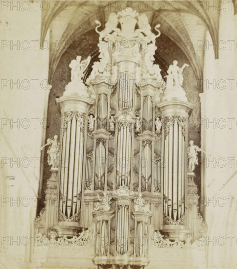 Organ Groote Kerk, Haarlem, Müller organ in the Sint-Bavokerk in Haarlem, stereograph, inscription: 'RBK', 1857 - 1863, photographer, pasteboard, paper, albumen print, height 87 mm x width 174 mm, church organ, Sint-Bavokerk (Haarlem), A tall ornate pipe organ fills the frame, with multiple tiers of vertical metal pipes framed by carved stone or wood columns and decorative moldings, cherubic and humanlike statues positioned on ledges and pedestals around the pipes, elaborate scrollwork and floral carvings crowning the upper sections, and arched architectural vaulting visible in the background above the instrument.