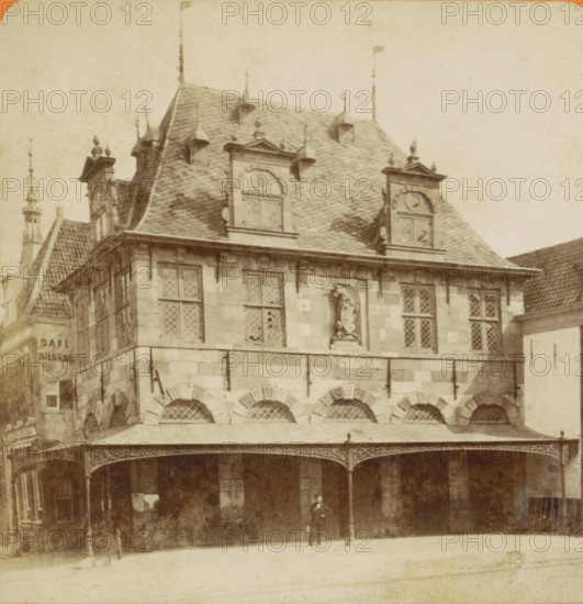 Horn. Roodenstein et le Waag, View of the Waag in Hoorn, Vues de Hollande, stereograph, inscription: '29', number: '1', Hoorn (North Holland), publisher: Léon & Lévy, Paris, publisher: J. Lévy & Cie, 1873 - 1890, photographer, pasteboard, paper, albumen print, height 87 mm x width 178 mm, weigh-house, Waag (Hoorn), A multi-story stone building with a steep tiled roof and decorative dormer windows occupies the image, featuring ornate gables, small finials along the roofline, and a statue set into a recessed niche on the upper facade; diamond-patterned window panes appear in rectangular windows, and a covered arcade with arched openings and ornate iron supports runs along the ground level, where a solitary figure stands beneath the canopy.