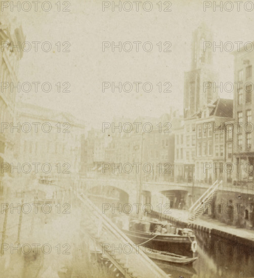The Old Canal., Canal dit Oude Gracht., Der alte Kanal., The old Canal, View of the Oudegracht in Utrecht, Utrecht, stereograph, Rotterdam, 1873 - 1890, photographer, pasteboard, paper, albumen print, albumendruk, height 88 mm x width 179 mm, city-view in general, 'veduta', canals, waters (in city), parts of church exterior and annexes: tower, Oude Gracht (Utrecht), A faded sepia-toned scene shows a canal edged by multi-story buildings with narrow façades and peaked roofs, a tall tower rising among them, arched bridges crossing the water, wooden staircases leading down to the canal, several moored boats with visible hulls and rigging, and faint details of windows and doors along the waterfront, all appearing softened and washed by age.