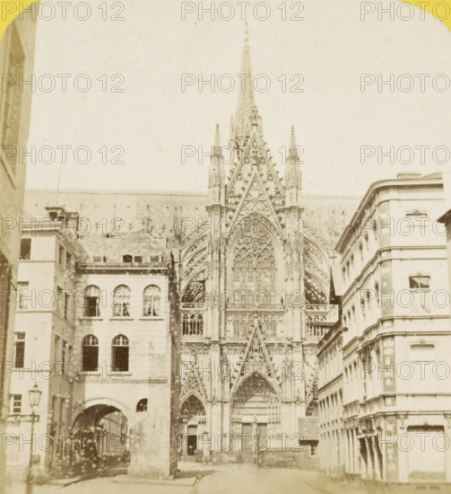Southern facade of Cologne Cathedral, Germany, Façade méridionale de la Cathédrale, Cologne (Prusse), Allemagne, stereograph, number: 'N. 552', inscription: 'Déposé.', inscription: '(Déposé)', photographer: Hippolyte Jouvin, 1864, North Rhine-Westphalia, pasteboard, paper, albumen print, height 87 mm x width 177 mm, urban housing, church (exterior), Cologne Cathedral, A sepia-toned photograph shows a tall ornate Gothic cathedral façade with pointed arches, intricate tracery, and a large central rose window flanked by spires, set between multistory stone buildings with arched and rectangular windows and decorative cornices, a street-level archway leading into a narrow passage on the left, a lamp post near the left foreground, and paving visible in the foreground.
