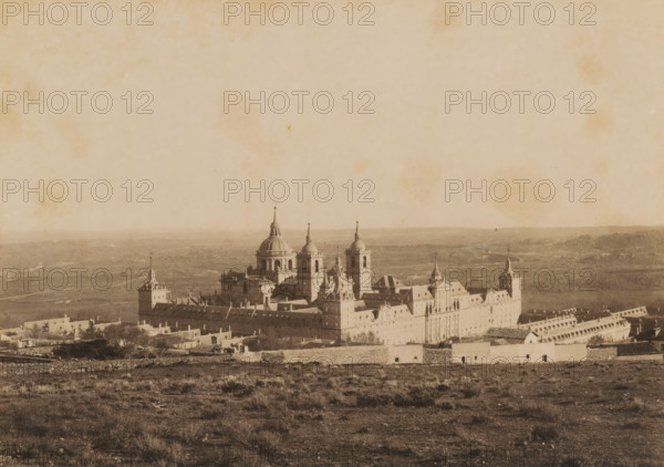 Escorial, el Monasterio desde la presa del Romeral, View of the Escorial near San Lorenzo de El Escorial, photograph, number: '2.', photographer: C. Huerta, San Lorenzo de El Escorial, 1860 - 1900, Comunidad de Madrid, pasteboard, paper, albumen print, height 316 mm x width 367 mm, abbey, monastery, convent, Roman Catholic church, palace, mausoleum, A wide, sepia-toned panorama showing a large stone building complex with multiple towers, domes, and spires centered in the middle ground, surrounded by low walls and smaller structures; the foreground consists of dry, grassy terrain with scattered shrubs and uneven ground; the distant background shows a flat, open landscape with faint hills along the horizon; the sky above is pale with mottled stains and spots.