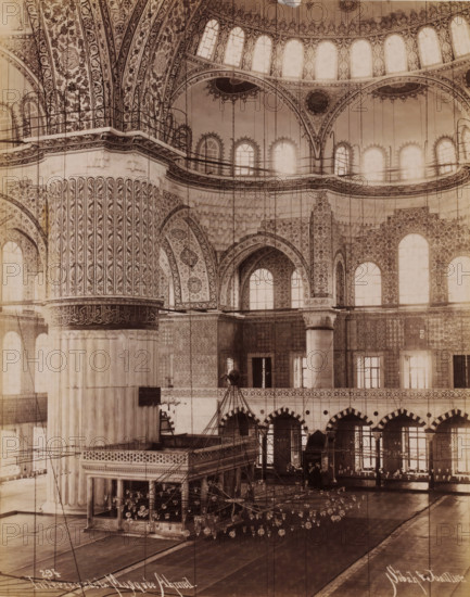 Intérieur de la Mosquée Ahmed, Interior of the Sultan Ahmet Mosque in Istanbul, photograph, number: '294', photographer: Sébah & Joaillier, Istanbul, 1888 - 1900, paper, albumen print, albumendruk, height 210 mm x width 264 mm, temple, shrine, Islam, Mohammedanism, Sultan Ahmet Mosque, The image shows an ornate interior space with large decorative columns and arches, intricate floral and geometric patterns covering walls and vaulted ceilings, rows of tall arched windows letting in light, suspended chains and many hanging glass lamps forming a chandelier arrangement, a raised ornate wooden or stone platform with carved balustrades, tiled lower walls with repeating motifs, a series of archways along a gallery, and polished floor surfaces reflecting light.