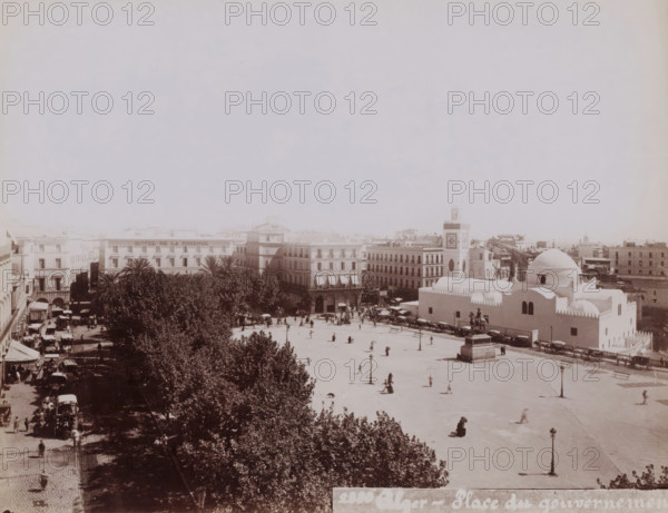 View of the place du Gouvernement (now the place des Martyrs) with the Djama?a el Djedid in Algiers on the right, Alger, place du gouvernement, photograph, number: '2330 ?', Algiers, 1860 - 1900, photographer, North Africa, paper, albumen print, height 188 mm x width 242 mm, temple, shrine, Islam, Mohammedanism, square, circus, Djama?a el Djedid, A wide sunlit plaza bordered by multi-story buildings and a row of trees sits in the lower part of the image, with people scattered across the open paved area and a few horse-drawn carriages and carts along the edges; a domed white building with smooth curved roofs and small arched windows occupies the right foreground, adjacent to a tower featuring a square face and circular decorative elements, while a statue on a pedestal stands near the dome and a street lined with shaded trees and parked carriages runs along the left side of the scene.