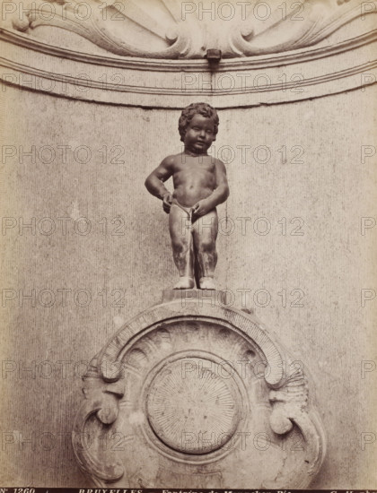 Fontaine de Manneken-Pis, Fountain of Manneken Pis in Brussels, Belgium, Bruxelles, photograph, number: 'No 1260', photographer: Gustave Hermans, Brussels, after sculpture by Jerôme Duquesnoy (II), 1884 - 1914, Jerôme Duquesnoy (II), after sculpture by, paper, albumen print, height 280 mm x width 215 mm, ornamental fountain, Manneken Pis, A stone statue of a naked child standing on a rounded pedestal, with curly hair and a neutral facial expression, positioned above an ornate carved circular relief; the child is depicted with one arm bent and the other hand touching the groin area, and a thin stream appears to flow downward from that point; the background shows a textured flat wall with horizontal molded bands and decorative scrollwork at the top and sides.