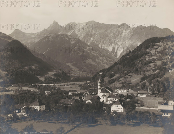 Schruns i. Montavontal, View of Schruns in the Montafon in Austria, photograph, number: '1264.', Schruns, 1900 - 1950, photographer, Montafon, paper, baryta paper, gelatin silver print, developing gelatin silver print, height 208 mm x width 264 mm, city-view in general, 'veduta', mountains, dale, valley, A sepia-toned panoramic view of a mountainous landscape with steep rocky peaks and forested slopes, a valley with scattered houses and farm buildings, and a village foreground dominated by a church with a bulbous dome tower; terraced fields and tree-lined meadows appear on the hillsides, narrow roads and paths wind between houses, and clusters of trees cast shadows across the open grassy areas.
