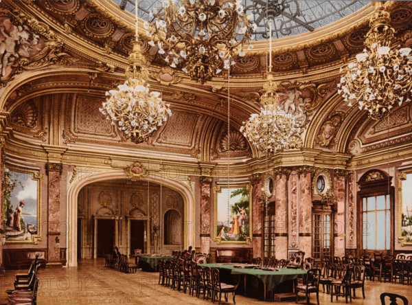 Casino de Monte Carlo, la nouvelle salle de jeu, Interior of the Monte Carlo Casino in Monaco, photomechanical print, number: '16478.', Monaco, cliché maker: Photochrom Zürich, Zürich (city), 1889 - c. 1920, photographer, paper, photochrom, height 166 mm x width 225 mm, casino, Monte Carlo, Monte Carlo Casino, A large ornate interior with a high domed ceiling featuring decorative moldings and painted panels, elaborate gilded chandeliers hanging from the ceiling, sculpted reliefs and ornate cornices along the upper walls, tall arched doorways and windows framed by carved pilasters, framed paintings set into the walls, long tables covered with dark cloths surrounded by many wooden chairs, patterned marble columns and decorative wall panels, a polished wooden floor and various carved wooden furnishings.