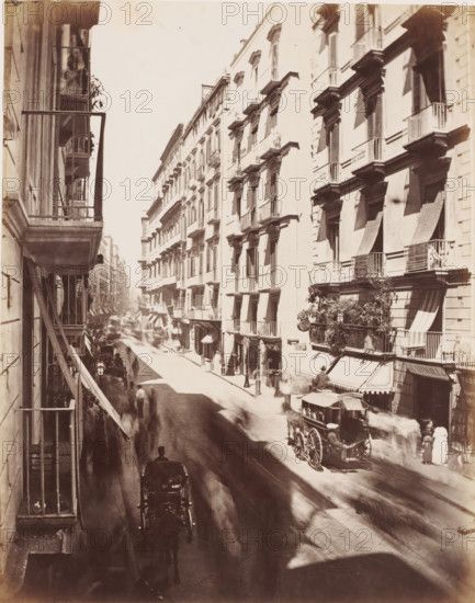 Naples rue Rôme Tolèdo, View of the Via Toledo in Naples, Italy, photograph, number: '12', number: '22.', Naples, 1851 - 1900, photographer, pasteboard, paper, albumen print, albumendruk, height 405 mm x width 306mm, street, Via Toledo, A sunlit narrow city street lined with tall multi-story buildings featuring shuttered windows and small wrought-iron balconies, some with awnings and plants, viewed from an elevated angle; horse-drawn carriages and blurred figures move along the cobbled roadway creating motion blur, with a carriage prominently visible in the foreground and another at the curb, while pedestrians stand near shopfronts and entrances beneath the balconies.