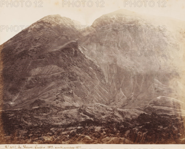 Le Vesuve Cratere 1873. grande overture 1872, View of the crater of Vesuvius after the eruption of 1872, Italy, photograph, number: '92.', number: 'No 4127', number: '11', photographer: attributed to Giorgio Sommer, Naples, 1873, Attributed to, pasteboard, paper, albumen print, height 305 mm x width 402 mm, volcano, Mount Vesuvius, A sepia-toned photograph shows a rugged mountainside with steep slopes and rocky textures, darker ridgelines contrasting with lighter eroded faces, scattered scree and patchy vegetation across the lower foreground, terraces and gullies cutting into the slopes, and a faint hazy sky above the peaks.