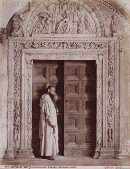 Porta in marmo di GA Amodeo, nel Chiostro piccolo, Monk standing in a marble portal in the monastery church Certosa di Pavia in Pavia, Italy, Certosa di Pavia, photograph, inscription: 'Brogi', number: '4641.', number: '13', Pavia (city), publisher: Giacomo Brogi, Florence, 1856 - 1881, photographer, Tuscany, Lombardy, pasteboard, paper, albumen print, height 404 mm x width 304 mm, monk(s), friar(s), parts of church exterior and annexes: portal, A man wearing a long robe stands in front of a large wooden door with raised rectangular panels, holding a large key in one hand and a smaller object in the other; the doorway is framed by an ornate carved stone surround with vertical decorative reliefs on either side and a horizontal carved lintel above, while an arched relief panel above the lintel depicts seated and kneeling figures carved in high relief within a semicircular arch.