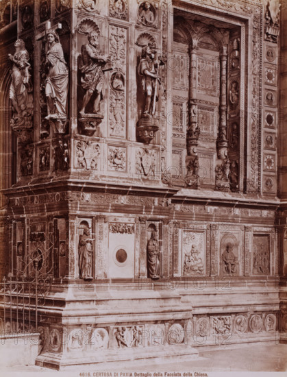 Dettaglio della facciata della Chiesa, Detail of the front of the monastery church Certosa di Pavia in Pavia, Italy, Certosa di Pavia, photograph, number: '13', number: '4616.', inscription: 'Brogi (t)', Pavia (city), publisher: attributed to Giacomo Brogi, Florence, after sculpture by anonymous, 1856 - 1881, photographer, after sculpture by, Tuscany, Lombardy, Attributed to, pasteboard, paper, albumen print, height 403 mm x width 304 mm, sculpture, church (exterior), A close view of a stone façade with carved panels and sculpted figures set into niches, showing multiple standing human figures in draped garments, relief scenes of people and animals, decorative floral and shell motifs, framed rectangular panels, carved columns with ornate capitals, and circular medallions along the lower band; the stone surface shows varied textures and weathering, and a metal gate with scrollwork appears at one corner.