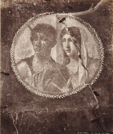 Photo reproduction of a fresco depicting Venus and Mars in Pompeii, Italy, Marte e Venere, Pompei, photograph, reproduction, number: '11', number: '81.', inscription: 'Mars et Venus, peinture, Pompei', Pompeii, after painting by anonymous, 1851 - 1900, photographer, pasteboard, paper, albumen print, height 406 mm x width 308 mm, (story of) Venus (Aphrodite), (story of) Mars (Ares), wall-covering, A worn circular fresco fragment shows two adjacent figures within a laurel-like border, one figure on the left with dark curly hair and a bare shoulder, the other on the right with long hair partly covered by a draped veil, both faces rendered in a faded, weathered style with visible cracks and surface abrasion across the image and darkened areas around the perimeter.