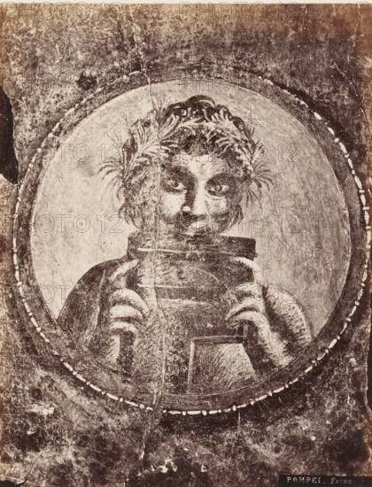 Fauno, Photo reproduction of a fresco depicting a faun, Pompei, photograph, reproduction, number: '11', number: '82.', Pompeii, after painting by anonymous, 1851 - 1900, photographer, pasteboard, paper, albumen print, albumendruk, height 400 mm x width 306 mm, picture, painting, wall-covering, satyrs, fauns, Sileni, A worn, monochrome image showing a circular framed portrait of a figure with tousled hair and laurel-like foliage woven into it, the face rendered with dark eyes and a faint smile, hands emerging from striped sleeves holding a rectangular object near the chest, surrounded by concentric circular bands and a textured, aged background with visible cracks, scratches, and spots.