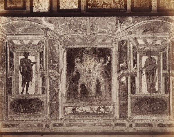 Photo reproduction of a fresco in Pompeii, Italy, photograph, reproduction, inscription: 'Parsi and bull, Pompei', number: '75.', number: '11', Pompeii, after painting by anonymous, 1851 - 1900, photographer, pasteboard, paper, albumen print, height 307 mm x width 403 mm, picture, painting, wall-covering, A faded mural panel showing architectural framing with columns and arches, flanked by two standing human figures in classical drapery within recessed niches, a central darkened scene with partially visible figures and raised arms, decorative smaller panels with animal and human motifs, ornamental moldings and rectangular compartments, and areas of surface wear, cracks, and discoloration across the painted surface.