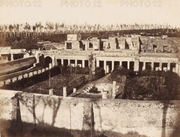 Remains of the Villa of Diomedes in Pompeii, Italy, photograph, number: '11', number: '49.', inscription: 'Pompei maison Diomede', Pompeii, 1851 - 1900, photographer, pasteboard, paper, albumen print, height 303 mm x width 402 mm, ruin of a building, architecture, A sepia-toned scene of an expansive ruined complex with stone walls, colonnades, arches, and rectangular openings, foregrounded by a high worn wall casting shadows, a central courtyard with short columns and circular stone remnants, a path leading through planted beds and trellised rows toward a colonnaded façade, and a backdrop of low stone structures and terraces topped by a line of thin, tall trees against a pale sky.