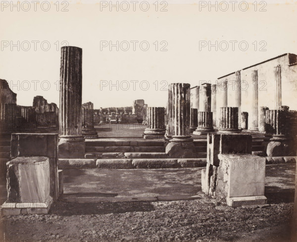 Ruins in Pompeii, Italy, Basilique prize du forum, 1818, Pompei, photograph, number: 'No. 4251.', number: '23', number: '10', number: '21', photographer: attributed to Giorgio Sommer, Pompeii, 1857 - 1875, Attributed to, pasteboard, paper, albumen print, albumendruk, height 304 mm x width 402 mm, ruin of a building, architecture, excavation, archaeology, A panoramic view of ancient stone ruins with multiple fluted columns of varying heights standing on raised stone platforms and bases, some columns intact and others broken into stumps; rectangular stone blocks and carved pedestals scattered in the foreground and along stepped platforms; a wide flat paved area beyond the columns leading to more ruined walls and low structures in the distance; a large wall with vertical grooves and an angled top running along the right side; textured ground with worn stone and gravel in the immediate foreground; an open sky occupying the upper portion of the image.
