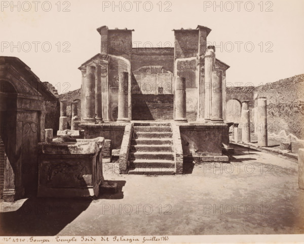 Ruin of the Temple of Isis in Pompeii, Italy, Temple Iside dit Pelasgia fouilles 1763, Pompei, photograph, number: '10', number: '30', number: '21', number: 'No 4210.', photographer: attributed to Giorgio Sommer, Pompeii, 1857 - 1875, Attributed to, pasteboard, paper, albumen print, height 307 mm x width 404 mm, ruin of a building, architecture, temple, shrine, Roman religion, Temple of Isis (Pompeii), A frontal view of an ancient stone structure with a central stepped platform leading up to a raised portico flanked by tall columns, some smooth and some fluted, with worn capitals and bases; the portico shows a partially preserved façade with rectangular wall panels and two small tower-like projections at the top; ruins and broken stone blocks occupy the foreground and sides, including carved stone sarcophagi and fragmented architectural elements; to the left a sculpted stone surface with decorative reliefs is visible, and to the right a row of standing columns and an arched opening in ...