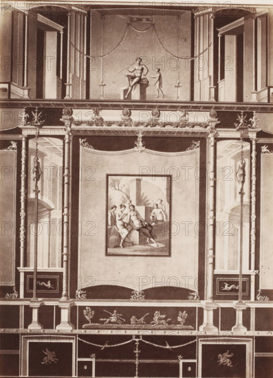 Photo reproduction of a fresco in Pompeii, Italy, photograph, reproduction, number: '84.', number: '11', Pompeii, after painting by anonymous, 1851 - 1900, photographer, pasteboard, paper, albumen print, height 403 mm x width 305 mm, picture, painting, wall-covering, A vertical section of an ornate wall with classical architectural details, featuring pilasters, columns, and decorative moldings. In the upper central panel, a framed scene shows a seated male figure holding a staff and a smaller standing figure nearby, with swags draped above. Below, a large rectangular panel contains a framed painting of several partially draped figures in a landscape setting. Flanking the central panels are tall niches and recessed doorways visible through vertical columns, with sculptural female figures mounted on tall staffs on either side. Ornamental friezes, medallions, and scrollwork run horizontally across the composition, while a lower register displays small sculptural figures engaged with anima...