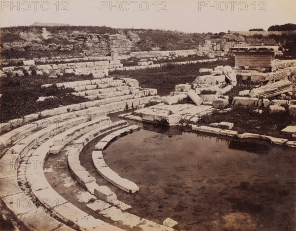 Siracuse Bagno di Diana, View of the ruins of the Bagno di Diana in Syracuse, Sicily, photograph, number: '2641', photographer: Giorgio Sommer, Syracuse (city), 1857 - 1914, paper, albumen print, albumendruk, height 199 mm x width 250 mm, landscape with ruins, A sepia-toned scene of stone ruins with curved stepped seating descending toward a shallow pool of water in the foreground, flat rectangular blocks and broken columns scattered on terraced stone platforms, low grassy areas and patches of vegetation between the masonry, a partially preserved stone structure with decorative molding on a raised platform to the right, and a low earthen bank with rough stone walls and shrubs along the back of the site under a pale sky.