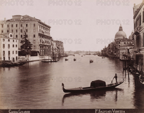Canal Grande, Gondolas and sailing ships on the Grand Canal in Venice, photograph, inscription: 'Venetie', photographer: Paolo Salviati, Venice, 1860 - 1870, pasteboard, paper, albumen print, albumendruk, height 197 mm x width 249 mm, height 276 mm x width 364 mm, canals, waters (in city), gondola, Grand Canal, A wide canal scene with several buildings lining both sides, featuring a row of multi-story structures with arched openings and windowed facades, a large domed church visible on the right skyline, and numerous small boats and gondolas floating on the water, one gondolier standing at the stern of a foreground gondola, wooden mooring poles along the edge of the canal, reflections of the boats and buildings on the water surface, and a distant waterfront visible toward the center background.
