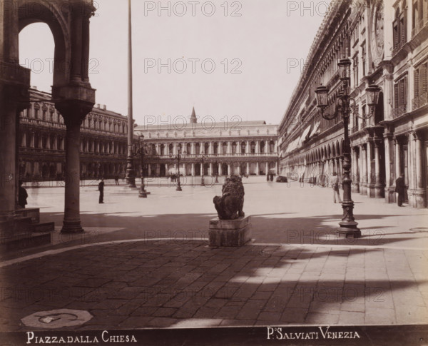 Piazza dalla Chiesa, View of St. Mark's Square from the Piazzetta dei Leoncini in Venice, photograph, inscription: 'Venetie', photographer: Paolo Salviati, Venice, 1860 - 1870, Paolo Salviati, photographer, pasteboard, paper, albumen print, albumendruk, height 199 mm x width 244 mm, height 276 mm x width 365 mm, square, circus, façade (or house or building), St. Mark's Square, Piazzetta dei Leoncini, A wide stone plaza framed by ornate arched buildings on either side with rows of columns and shuttered windows, an elevated colonnade visible across the open space, a stone lion statue on a plinth facing away from the viewer near the center foreground, tall decorative lampposts with ornate metalwork standing along the plaza, scattered figures standing or walking, shadows cast on the paved ground, and architectural details such as balustrades, cornices, and awnings along the building facades.