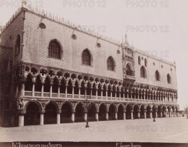Façade of the Doge's Palace in Venice, Pal.zo Ducale Facciata sulla Piazzetta, photograph, inscription: 'Venetie', photographer: Paolo Salviati, Venice, 1860 - 1870, Paolo Salviati, photographer, pasteboard, paper, albumen print, albumendruk, height 198 mm x width 250 mm, height 276 mm x width 364 mm, facade (or house or building), Doge's Palace, A large pale stone building with ornate architectural details fills most of the image, showing a facade with two tiers of arched openings supported by columns and decorative circular tracery above the lower arches; the upper wall displays tall arched windows with mullions and small circular window features set into a patterned brick surface, and a row of pointed ornamental pinnacles runs along the roofline; a prominent sculptural balcony and decorative sculptures are visible on the right section of the facade, and a statue stands at a corner near the center right; the foreground shows a broad open paved area with a solitary lamp post and the l...