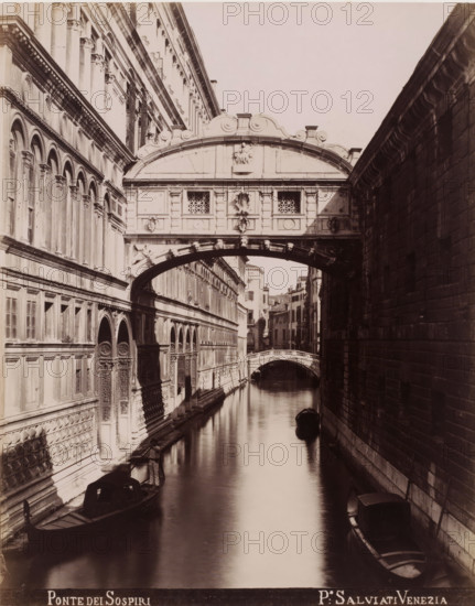 Ponte dei Sospiri, Bridge of Sighs in Venice, photograph, inscription: 'Venetie', photographer: Paolo Salviati, Venice, 1860 - 1870, pasteboard, paper, albumen print, albumendruk, height 251 mm x width 198 mm, height 365 mm x width 276 mm, bridge in city across river, canal, A narrow canal bordered by tall stone buildings with ornate facades and arched windows runs into the distance beneath a decorated enclosed bridge spanning the water, the bridge featuring carved panels and small lattice windows and sitting above a curved stone arch; gondolas float on the calm reflective water with one positioned near the foreground and another further back, and a person stands in a gondola along the left edge near a building entrance; the right building shows a textured masonry wall in shadow while the left building displays rows of arches, pilasters, and carved doorways, and a smaller arched pedestrian bridge is visible farther down the canal.