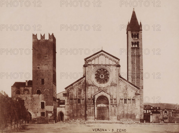 Verona- S. Zeno, Exterior of the Basilica of San Zeno in Verona, Italy, photograph, number: '13', number: '9', Verona, 1851 - 1900, photographer, pasteboard, paper, albumen print, height 305 mm x width 405 mm, church (exterior), parts of church exterior and annexes: campanile, Basilica of San Zeno, A large stone church facade with a central rose window and a decorated arched main doorway flanked by columns, a triangular pediment above the entrance, and vertical rows of narrow windows; to the right a tall narrow bell tower with arched openings near its top and a pointed roof; to the left a square brick tower with crenellated top and small arched openings, adjoining lower stone and brick buildings; an open paved foreground and a row of trees visible at the left edge.