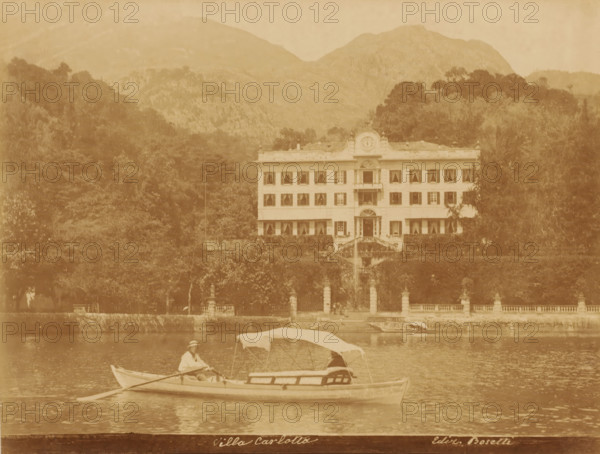 Villa Carlotta, Villa Carlotta on Lake Como, Tremezzo, Italy, photograph, publisher: Bosetti, 1851 - 1900, photographer, Lombardy, pasteboard, paper, albumen print, height 348 mm x width 455 mm, villa, lake, rowing facing backward, pulling, Lake Como, A sepia-toned photograph shows a large multi-story villa with symmetrical rows of windows and a central entrance flanked by stairways, set behind a tree-lined terrace and balustrade; in front of the villa a body of water reflects the scene and a small rowboat with a partially covered canopy floats on the water, carrying two people, one seated at the oars wearing a hat, with wooded hills and mountains rising in the background.
