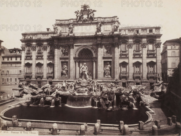 Fontana di Trevi (Roma), View of the Trevi Fountain in Rome, Italy, photograph, number: 'No 1044.', address: 'EDMONDO BEHLES, STUDIO MARIO DEL FIORI 28, MAAZZINO CORSO 196, ROMA', number: '26', photographer: Edmondo Behles, Rome, 1859 - 1866, pasteboard, paper, albumen print, height 309 mm x width 378 mm, ornamental fountain, Trevi Fountain, A wide frontal view of an ornate stone building with a large sculptural fountain in front, showing a semicircular basin of dark water edged by a low balustrade and stone posts, an array of carved figures and rocky formations with water cascading over them into the basin, and a central prominent statue among other statues set into niches framed by tall columns on the building facade; the multi-level facade has decorative reliefs, pilasters, arched windows, and a large central arch with a lattice pattern, topped by an elaborate sculptural crest and additional standing statues along the roofline, while flanking buildings and a narrow street are visibl...