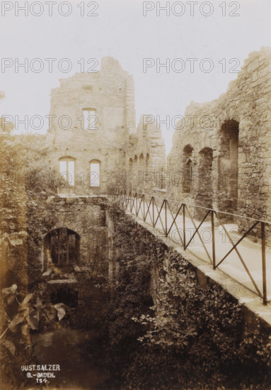 Ruin of Hohenbaden Castle, photograph, inscription: 'Gust. Salzer, B.-Baden., 154.', date: '1902', photographer: Gustav Salzer, Baden-Baden, 1902, Baden-Württemberg, paper, baryta paper, daylight collodion silver print, height 166 mm x width 116 mm, ruin of a dwelling, house, castle, A sepia-toned photograph showing the stone ruins of a building with a long narrow walkway edged by a metal railing running alongside a high stone wall with arched openings, a taller ruined facade with rectangular window openings at the far end, overgrown vegetation and ivy clinging to the lower walls and ground below, and a dark arched doorway or opening at the base partially obscured by foliage.