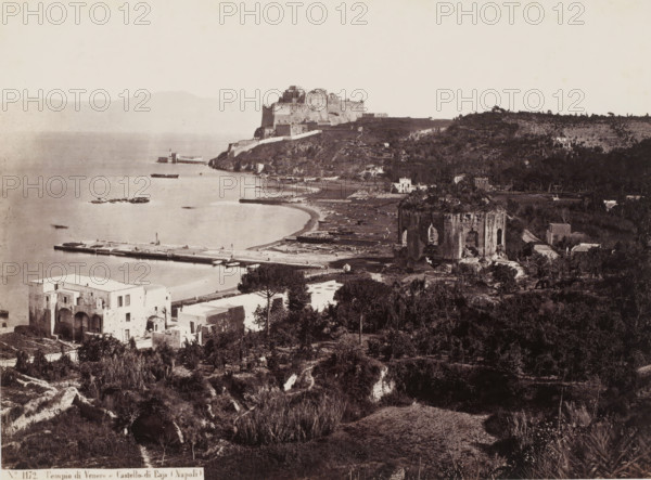 View of the Bay of Naples, Italy, Tempio di Venere e Castello di Baja Napoli, photograph, number: 'No. 1172.', address: 'GIORGIO SOMMER, STUDIO MONTE DI DIO 4., MAGAZZINO S. CATERINA 5., NAPOLI', photographer: Giorgio Sommer, Naples, 1857 - 1914, pasteboard, paper, albumen print, albumendruk, height 306 mm x width 375 mm, gelding of a building, architecture, gulf, bay, fortress, A wide coastal panorama showing a body of calm water with a long pier extending into it and small boats moored nearby, a curved shoreline with a narrow beach, a large fortress-like structure perched on a headland above the shore, terraces and dense vegetation covering hillsides, multiple stone and stucco buildings of varying sizes scattered among trees, a prominent ruined tower or cylindrical stone structure near the shoreline with visible openings and weathered surfaces, agricultural plots and rows of planted terraces on the distant hillside, and a foreground of shrubs, low trees, and uneven ground leading dow...
