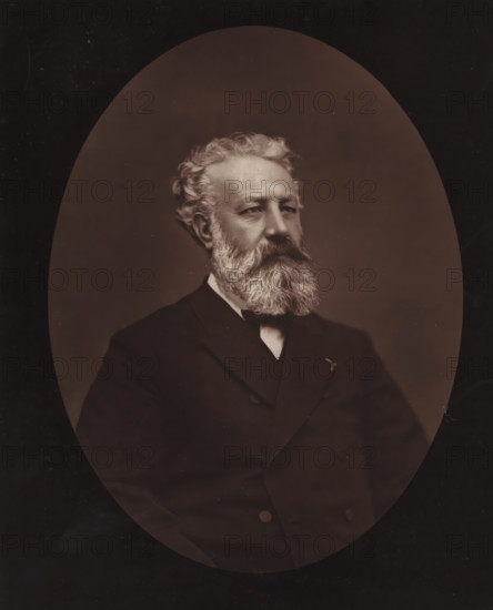Portrait of Jules Verne, Jules Verne, page, photomechanical print, inscription: 'Galerie Contemporaine, 126, boulevard Magenta. - Paris., Né à Nantes, le 8 février 1828.', photographer: Étienne Carjat, cliché maker: Goupil & Cie., c. 1873 - in or before 1878, paper, Woodburytype, height 231 mm x width 186 mm, Person, historical persons, adult man, An oval-framed sepia portrait of an older man shown from the chest up wearing a dark double-breasted suit, a white shirt collar, and a dark bow tie, with a full, bushy white beard and mustache, wavy white hair swept back, a solemn facial expression, and a softly lit neutral background.