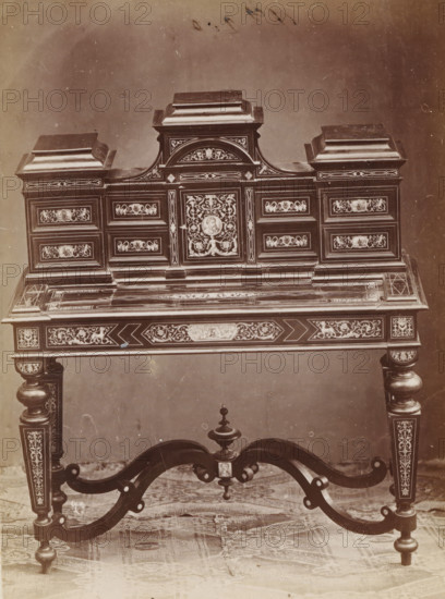 Writing table with inlay, No 23 Scrivania, photograph, page, inscription: 'Alta, 133. Larga, 118. Fonda, 58.', inscription: 'Ia 350', c. 1878 - c. 1885, photographer, paper, albumen print, height 127 mm x width 95 mm, Photo on unnumbered page., writing-table, writing-desk, A decorative wooden desk with an ornate upper section featuring raised panels and embellished rectangular compartments, each panel filled with intricate floral and scrollwork inlays and medallion-like circular designs; the central upper portion has a curved pediment and a prominent rectangular door with elaborate inlaid foliage surrounding a round portrait-like motif, flanked by symmetrical drawers with matching inlay work; the flat writing surface shows linear and geometric inlaid patterns and is bordered by ornamental trim; the apron beneath the surface carries further detailed inlay and carved motifs; turned legs with carved and inlaid panels descend to rounded feet and are connected by curved stretcher supports t...
