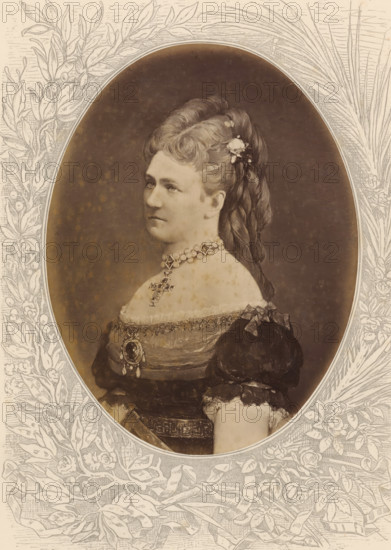 Karoline, Queen of Saxony, Photo reproduction of a painted portrait of Carola, photograph, reproduction, page, after painting by anonymous, c. 1875 - in or before 1880, photographer, paper, albumen print, height 189 mm x width 143 mm, Photo on unnumbered page., Person, Carola (Queen of Saxony), historical persons - BB - woman, queen, empress, etc. (wife of a ruler), A sepia-toned oval portrait of a woman shown in profile from the chest up, set within an ornate floral and leaf engraved border. The woman has hair swept up and braided with a small cluster of flowers pinned near the crown, and she wears a high beaded choker necklace with a pendant and a decorative cross suspended below it. Her dress has puffed sleeves, lace trim at the neckline, and a brooch or medallion at the bodice with additional ribbons and ornamental details. The background inside the oval is plain and darker, while the surrounding border is filled with engraved leaves, flowers, and flowing ribbon motifs.