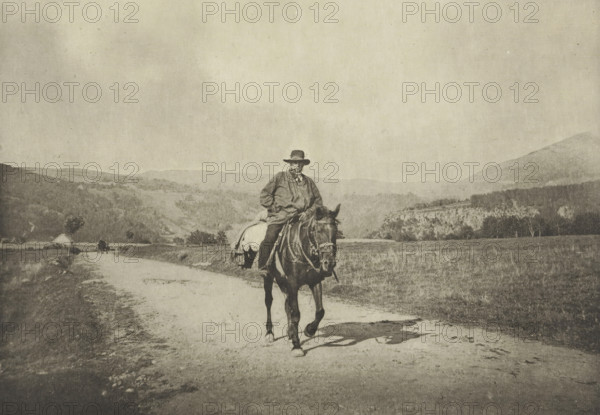 Horse rider on a country road, Mont-Dore, Retour du Moulin (Mont-Dore), photomechanical print, photographer: G. de Magnitot, cliché maker: Fillon & Heuse, printer (person): Charles Wittmann, Paris, c. 1891 - in or before 1896, printer (person), paper, photoaquatint, height 130 mm x width 186 mm, riding a horse, ass, or mule, rider, horseman, (high) hill, A sepia-toned scene shows a figure wearing a wide-brimmed hat and loose outerwear sitting astride a horse on a dirt road, the horse facing the camera with tack and a blanket visible; the road runs away into the distance past grassy fields and low trees, with rolling hills and a distant treeline under a wide, pale sky.