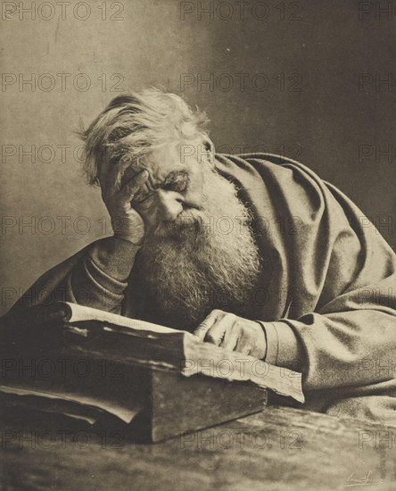 Portrait of an unknown old man with a book, L'Étude, photomechanical print, photographer: Edmond Sacré, cliché maker: Fillon & Heuse, printer (person): Charles Wittmann, Paris, c. 1891 - in or before 1896, Edmond Sacré, Fillon & Heuse, Charles Wittmann, photographer, cliché maker, printer (person), paper, photoaquatint, height 211 mm x width 170 mm, historical persons not known by name, reading, scholar, philosopher, beard, An older man with long hair and a full beard rests his head on one hand while leaning over an open book, wearing a heavy draped garment with visible folds, his other hand touching the pages, all shown in a monochrome, high-contrast image with a plain background.