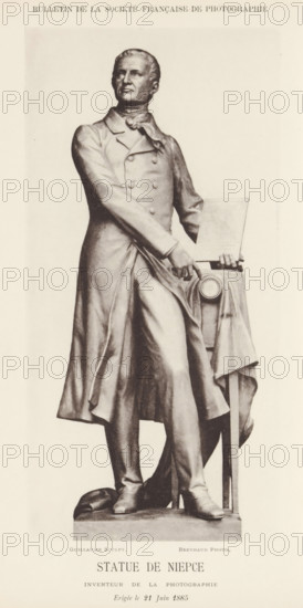 Statue de Niepce, inventeur de la photographie, Statue of Joseph Nicéphore Niépce, page, photomechanical print, inscription: 'Erigée le 21 juin 1885', photographer: Michel Berthaud, cliché maker: anonymous, after sculpture by Eugène Guillaume, 1885, Eugène Guillaume, after sculpture by, paper, collotype, photoprint, height 187 mm x width 92 mm, Person, Joseph Nicéphore Niépce, piece of sculpture, reproduction of a piece of sculpture, historical persons, camera, photography, invention, discovery, science and technology, Châlon-sur-Saône, A tall monochrome statue of a man standing on a rectangular plinth, dressed in a long double-breasted coat with a high collar and a tied neckcloth, one arm crossed at the waist and the other resting on a small draped table beside him; the table holds a rectangular flat object and shows a circular medallion on its cloth, and the man’s gaze is directed slightly upward with a composed facial expression and neatly styled hair, while his legs are positioned ...
